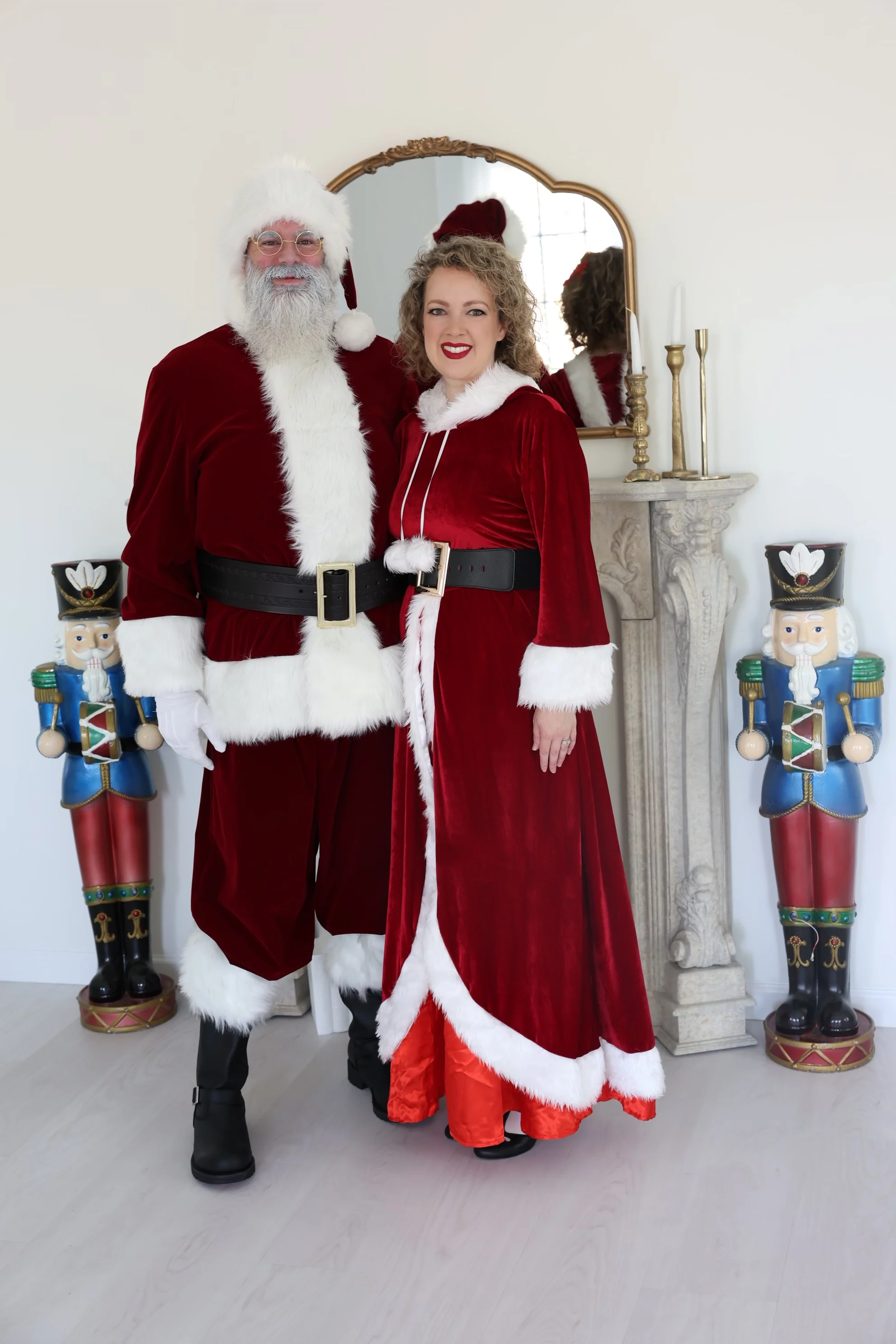 Santa and Mrs. Claus standing together in burgundy velvet beside the fireplace